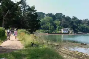 Sentier côtier sur l'île aux Moines avec des promeneurs longeant une maison typique bretonne et une végétation verdoyante.
