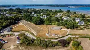 Vue aérienne de Locmariaquer avec un site mégalithique, des maisons traditionnelles, et la mer en arrière-plan. ​​





